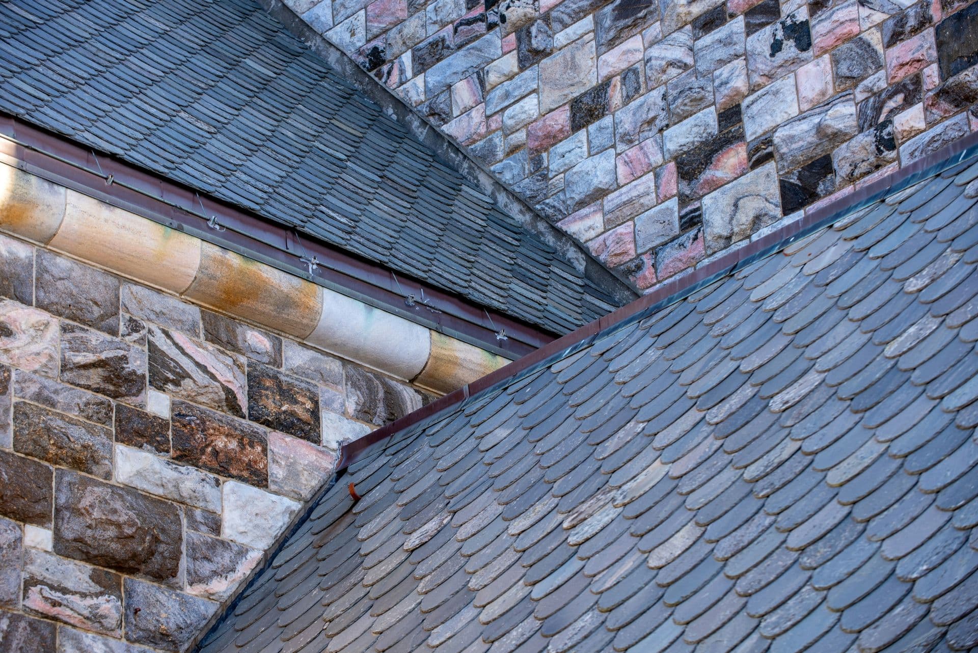 Intersecting portions of a slate tiled roof on a stone brick building.